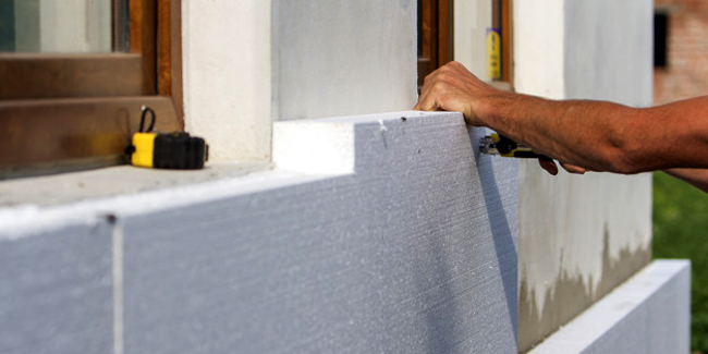 Worker hand with level and knife measuring and cutting white rigid polyurethane foam sheet on wall at newly installed plastic window. Modern technology, renovation, insulation concept.